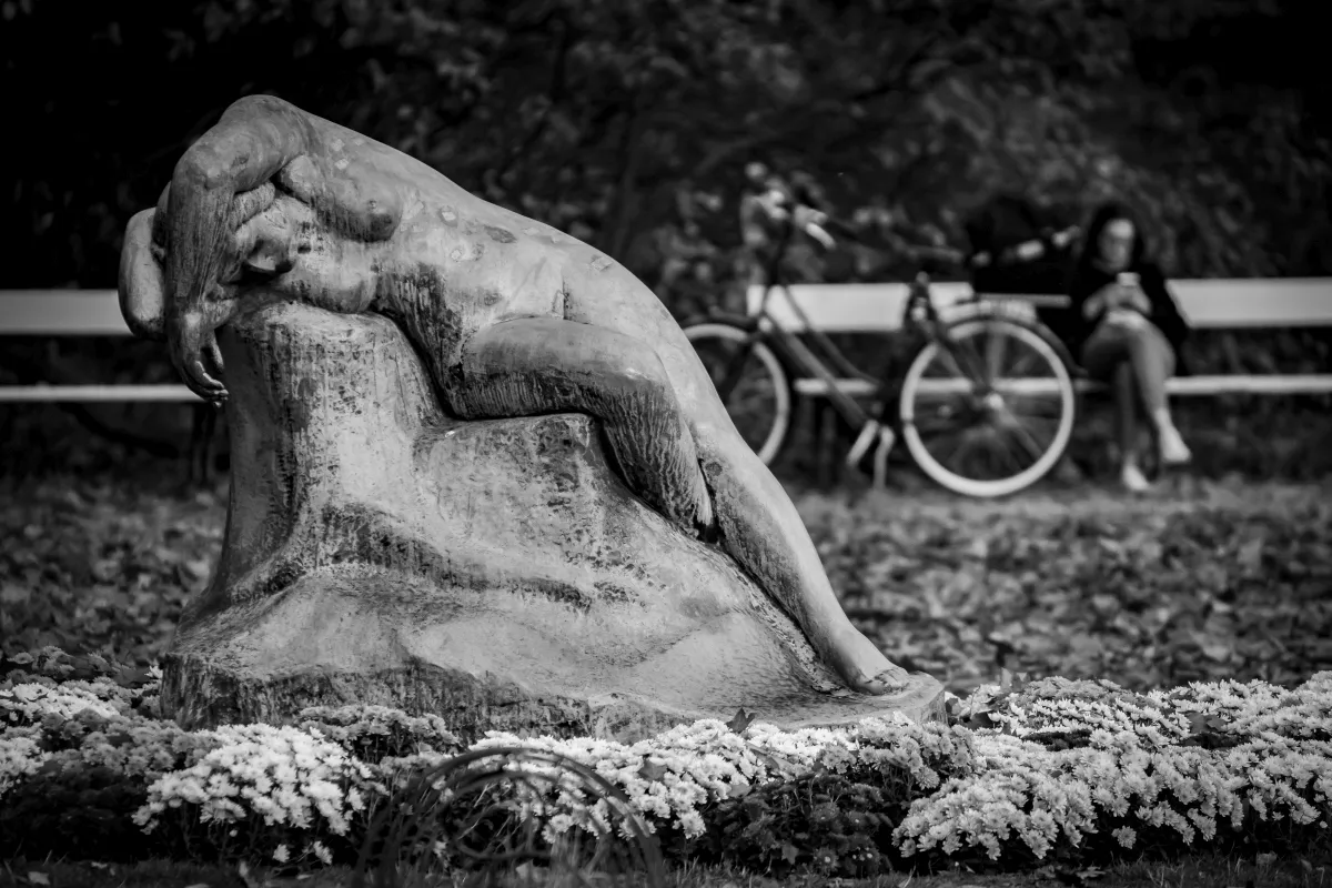 Reclining sculpture beside a bench and a bicycle